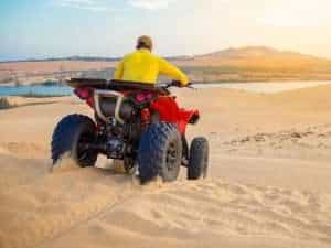 Tourist riding a quad bike through the Hurghada desert with sunset and Bedouin tents in the background – Egypt Breeze Tours