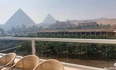 Panoramic view of the Giza Pyramids from a modern balcony overlooking the desert in Cairo, Egypt