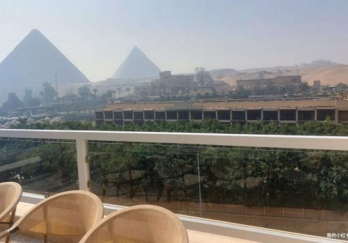 Panoramic view of the Giza Pyramids from a modern balcony overlooking the desert in Cairo, Egypt